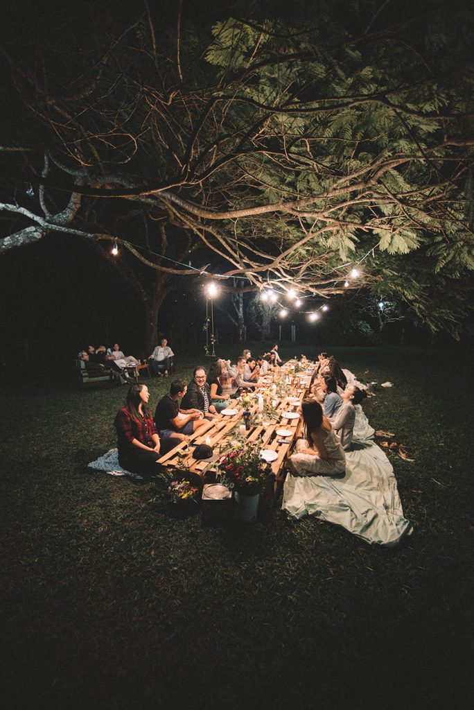 Image of friends gathering around a pallet table in the grass for a birthday party.