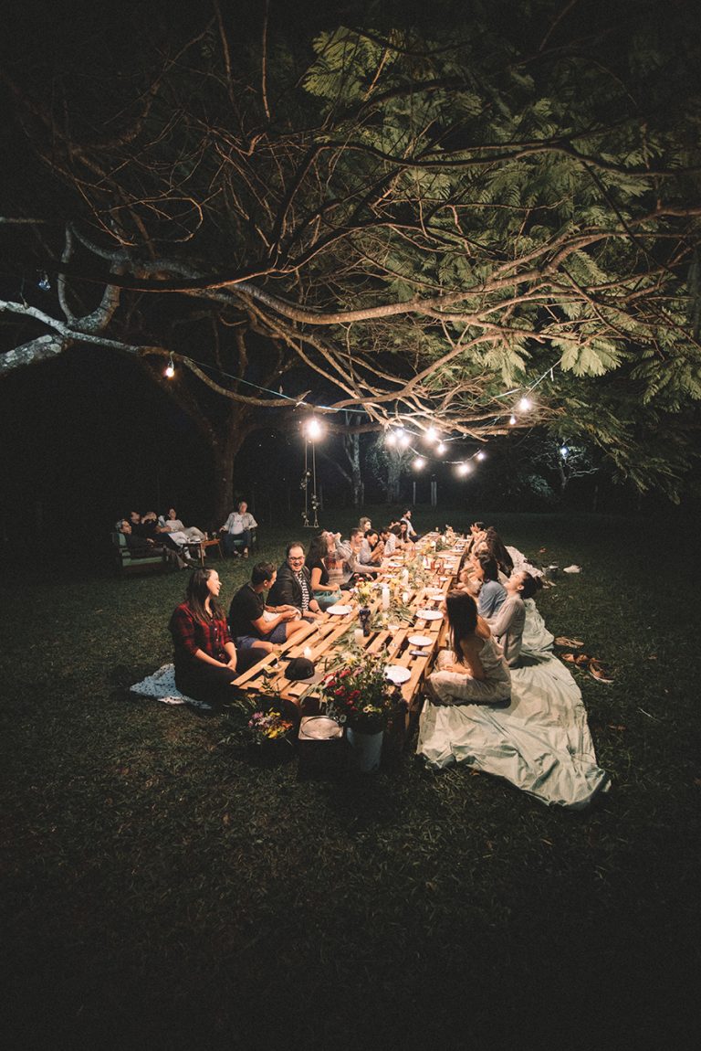 Image of friends gathering around a pallet table in the grass for a birthday party.